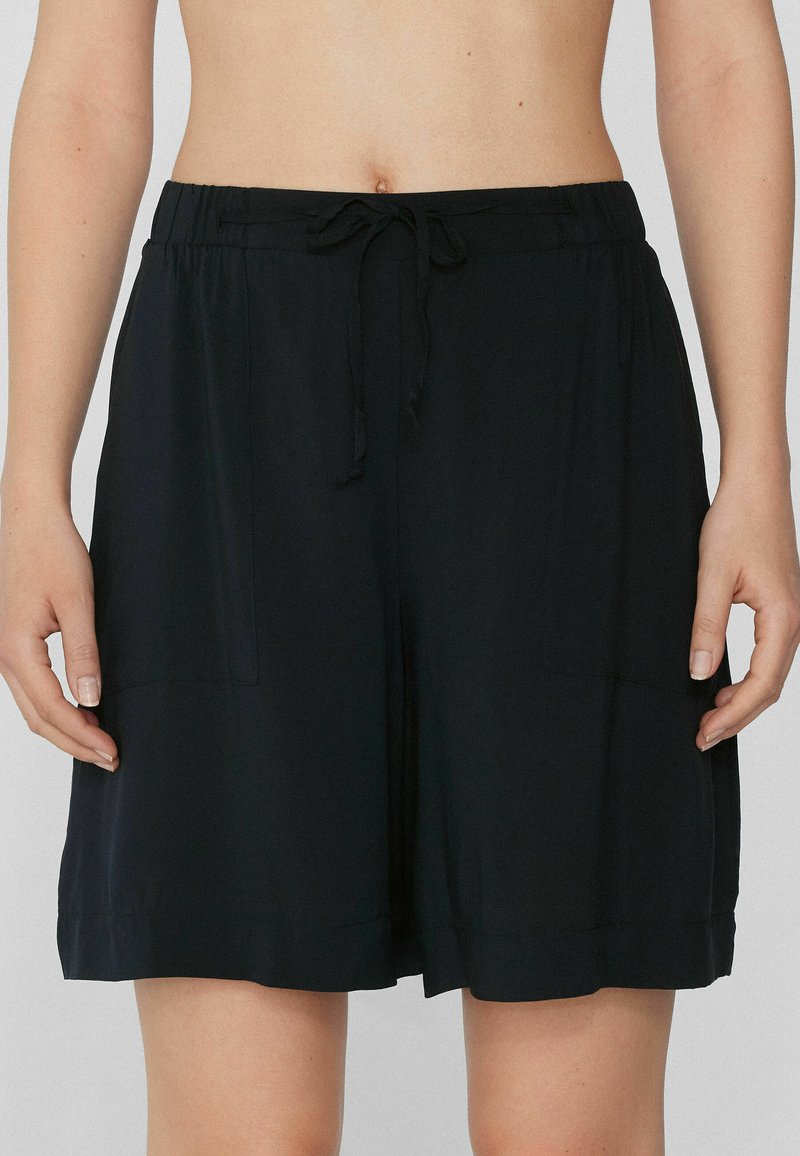 Pantalones cortos negros de tela suave, con una cinturilla elástica y cordón, y dos bolsillos laterales. Textura suave y corte holgado.
