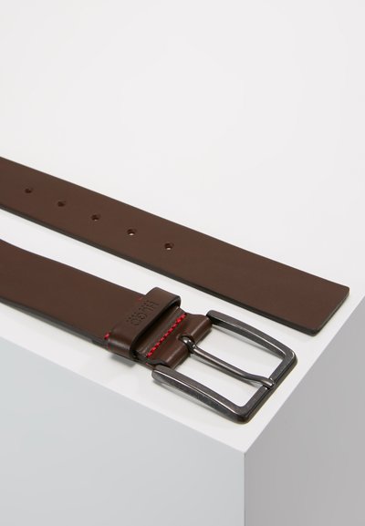 Ceinture en cuir marron avec une boucle en métal argenté, présentant une touche de rouge et plusieurs trous pour l'ajustement. Texture lisse et forme rectangulaire.