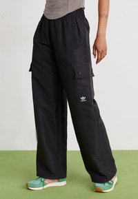 Mustad mustused cargo püksid, mis on valmistatud kergest kangast, elastse vöökoha, küljetaskute ja Adidas logo kujutisega vasakul jalal.