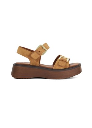 Sandales à plateforme en daim tan avec une sangle de cheville réglable, des accents de boucles et une semelle texturée en bois. Talon plat avec une légère courbure.