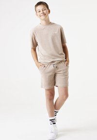 Conjunto de camiseta y pantalones cortos de tela de rizo beige, que presenta un cuello redondo, mangas cortas, bolsillos laterales y zapatillas blancas con calcetines de estampado.