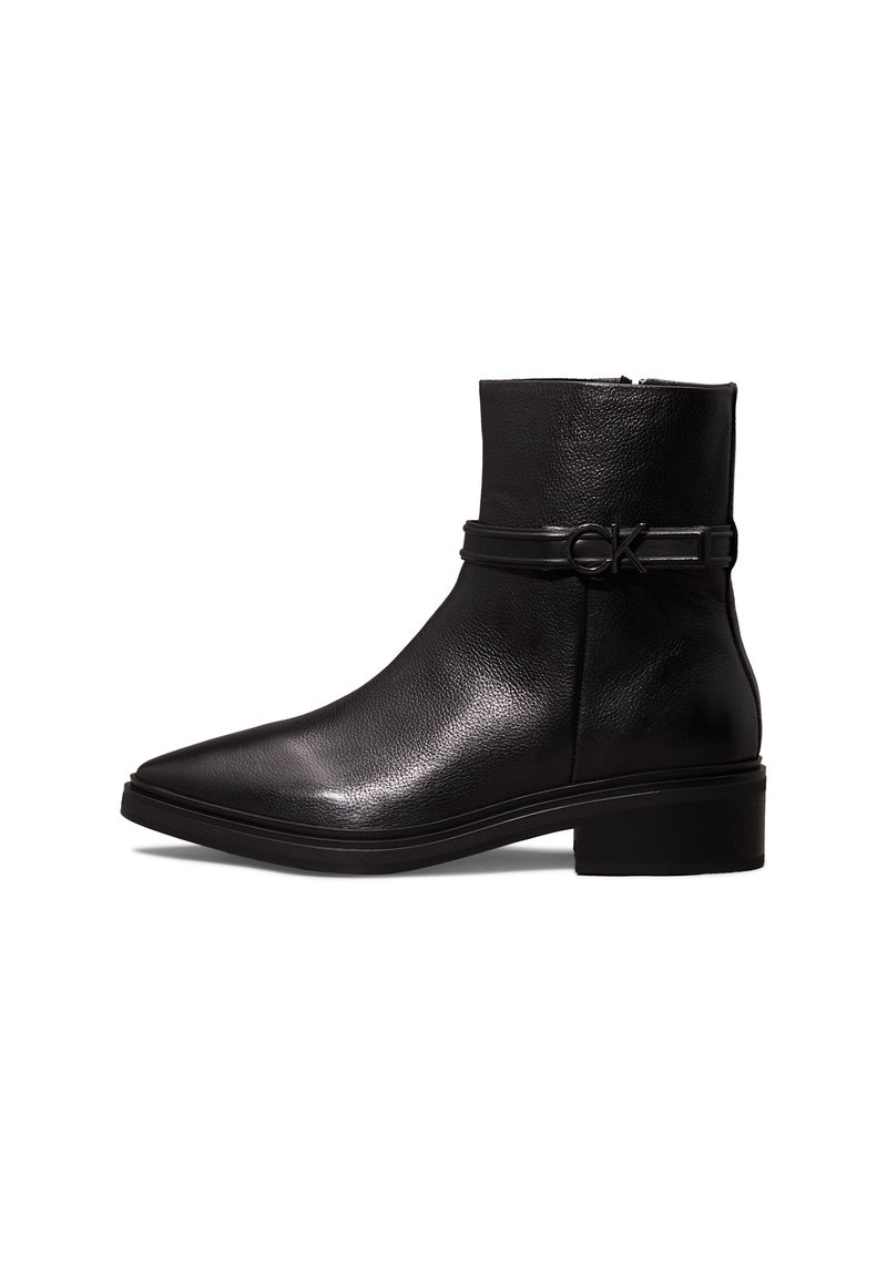 Bottines en cuir noir avec un bout pointu, fermeture éclair, et une sangle décorative avec une boucle circulaire. Design à petit talon carré.
