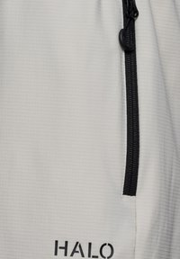 Biały teksturowany materiał z pionowym czarnym zamkiem błyskawicznym i czarnym logo „HALO” w pobliżu dolnej krawędzi.