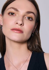 Srebrne kolczyki w kształcie serca, delikatny srebrny naszyjnik i gładka, ciepła skóra w kontrastującym ciemnym topie o rypsowej fakturze.