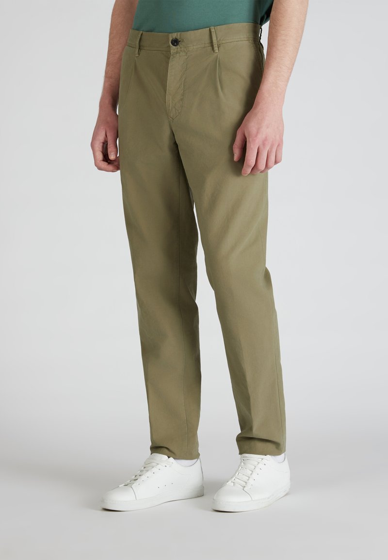 Olijfgroene chino's met een slim fit, voorzien van steekzakken, een rits en een enkele knoopsluiting, gecombineerd met witte sneakers.