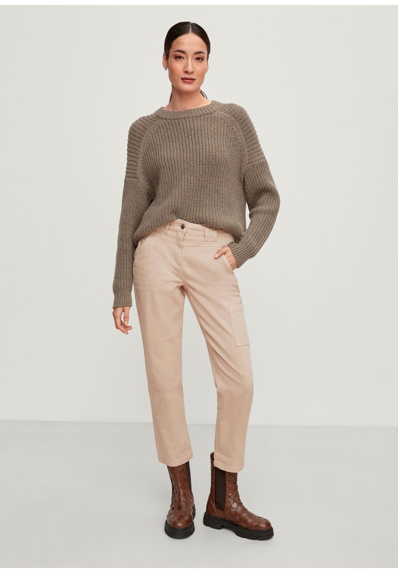 Maglione lavorato a maglia color khaki con texture a costine, abbinato a pantaloni cargo beige chiaro con tasca laterale e stivaletti alla caviglia intrecciati marroni.