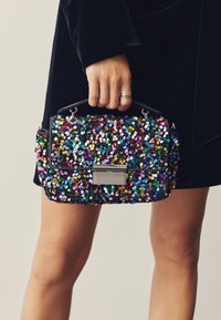 Rankinė su blizgučiais, juodos spalvos pagrindu, marginti blizgučiais, stačiakampio formos, trumpa rankena ir sidabrinės detalės priekyje.