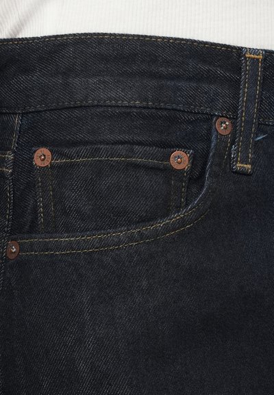 Tmavomodré džínsové nohavice s medenými nitmi, žltým prešitím a detailom malého vrecka. Hladká textúra, strih s rovnými nohavicami.