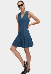 Dżinsowa sukienka z dopasowanym korpusem, dekoltem w kształcie litery V, zapinana na guziki z przodu i z rozkloszowanym dołem. Posiada boczne kieszenie i ma długość do kolan, w średnim niebieskim odcieniu.