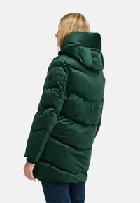 Abrigo verde esponjoso con capucha, que presenta una tela texturizada, un patrón de acolchado horizontal y un logo redondo en la manga izquierda.