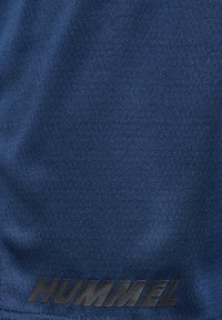 Mörkblått tyg med en texturerad mönstring, med en framträdande svart "HUMMEL"-logotyp längst ner. Mjukt, atletiskt material.