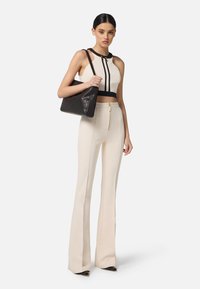 Top corto bianco con accenti neri, abbinato a pantaloni larghi color crema. Una borsa in pelle nera completa l'outfit. Texture lisce, dettagli con zip.