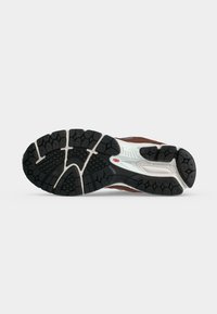 Σόλα αθλητικού παπουτσιού New Balance με μαύρο πέλμα, λευκή ενδιάμεση σόλα και κόκκινη λεπτομέρεια με λογότυπο, απομονωμένη σε ανοιχτό γκρι φόντο.