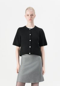 Black knitted short-sleeve cardigan with a round neckline and white buttons, paired with a gray A-line skirt. Smooth texture, minimal design.