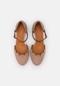 Ballerines en daim beige avec bords festonnés et une bride en cuir marron perforé. Semelle intérieure texturée avec un motif ondulé. Style fermé à l'avant.