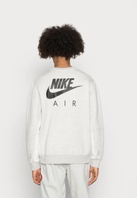 Harmaa huppari, jossa on pyöreä kaula-aukko ja suuri musta "NIKE" -logo sekä "AIR"-teksti selässä. Vahvistetut hihansuut ja helma.