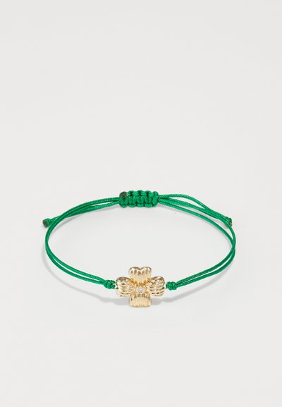 Pulsera de cordón ajustable verde con un charm en forma de flor dorada que presenta detalles acanalados y un cristal claro en el centro.