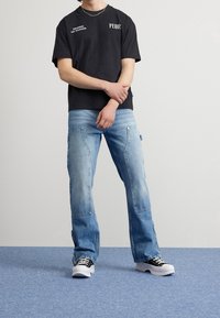 Camiseta negra de manga corta con texto blanco, combinada con jeans de mezclilla azul claro con un acabado desgastado y detalles de costura visibles.