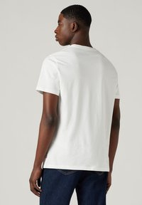 Hvid kortærmet t-shirt lavet af bomuld med rund halsudskæring. Sætter sammen med mørke denim jeans, set fra ryggen.