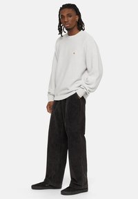 Sudadera gris claro con cuello redondo y un pequeño logo, combinada con pantalones de pana negros de corte holgado. Zapatillas negras completan el look.