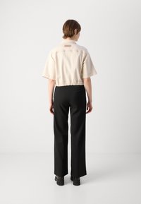 Beige kortjacka med korta ärmar, elastisk midja och logotyp-patch på ryggen, parat med svarta vida byxor och platåstövlar.