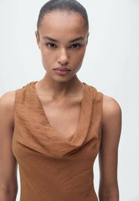 Cowl-neck sleeveless dress in a warm brown fabric, featuring a smooth texture and subtle drape, accentuating the neckline and shoulders.