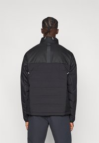 Μαύρο μπουφάν με επένδυση, διαθέτει ψηλό γιακά, δομημένους ώμους και κομψές οριζόντιες ραφές. Αντανακλαστική λεπτομέρεια στο πίσω μέρος.