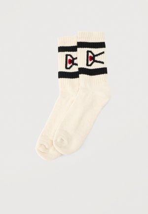 Paire de chaussettes mi-mollet couleur crème, à rayures noires et ornées de motifs rouges, noirs et blancs sur les bordures, présentée sur un fond clair.