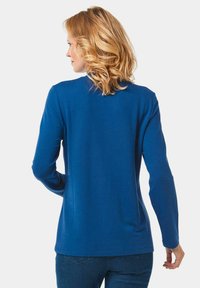 Blaues Langarmhemd aus weichem Stoff, mit rundem Halsausschnitt und geradem Saum, getragen mit Jeans, zeigt eine glatte Rückansicht.