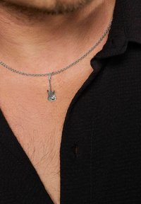 Collana in argento con pendente a forma di chitarra elettrica in miniatura, caratterizzata da un design dettagliato e una texture liscia, indossata su una camicia nera.