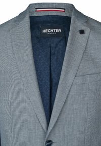 Grijze geblokte blazer met een marineblauwe voering, voorzien van een subtiel H-patroon. Inclusief een enkele knop en detail van een borstzak.