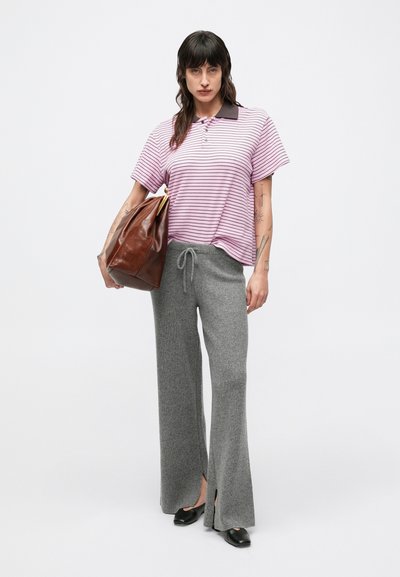Pruhované ružové a biele polo tričko s tmavým golierom, skombinované s bledosivými nohavicami so širokými nohavicami. V ruke hnedá kožená taška. Čierne topánky.
