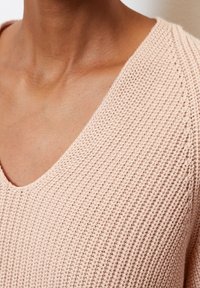 Pull en maille rose clair avec un col en V, présentant une texture côtelée et un tissu doux et respirant, idéal pour une tenue décontractée.