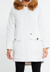 White parka jacket with a faux fur collar in orange-brown, front pockets with button closures, and a straight cut without a hood.