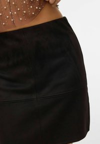 Gonna mini in finta suede nera con una texture liscia e linee pulite. Presenta un taglio semplice ed è progettata per sedersi in vita.