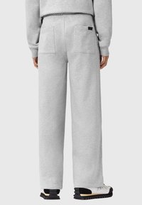 Helle graue Sweatpants mit einer lockeren Passform, ausgestattet mit zwei Gesäßtaschen und einem elastischen Bund, kombiniert mit schwarz-weißen Schuhen.