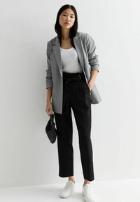 Grå blazer, vit linne, svarta högmidjade byxor med knytbälte och vita sneakers. Svart flätad handväska ger textur.