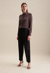 Camicia nera a maniche lunghe con un motivo floreale, abbinata a pantaloni neri a vita alta e sandali neri con tacco. Tessuto dalla consistenza liscia.