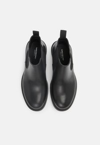 Bottines en cuir noir avec panneaux latéraux élastiques et languettes, vues de dessus sur un fond clair uni.