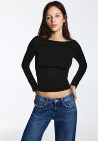 Zwart lang mouwen top met een aansluitend ontwerp, gecombineerd met high-waisted blauwe spijkerbroek met decoratieve studs op de zakken.