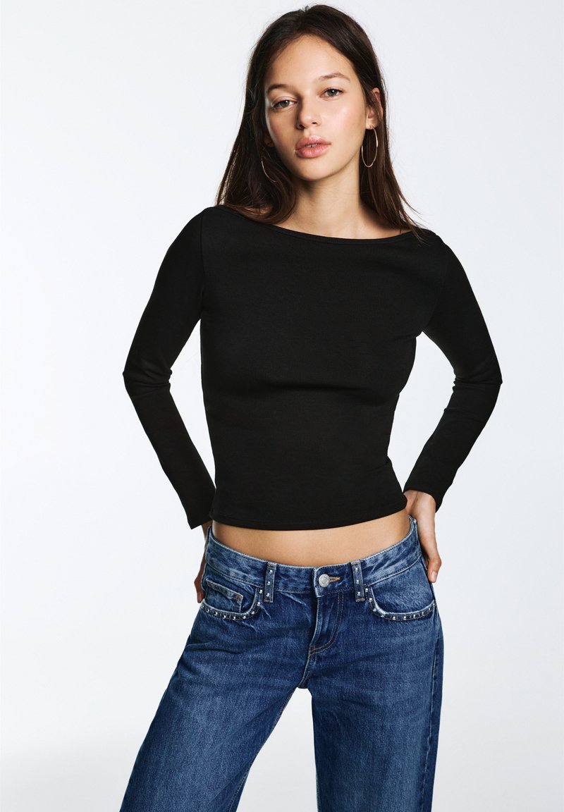 Zwart lang mouwen top met een aansluitend ontwerp, gecombineerd met high-waisted blauwe spijkerbroek met decoratieve studs op de zakken.