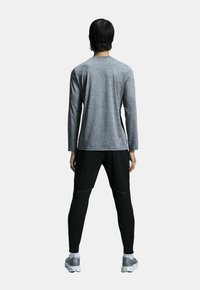 Grå langærmet skjorte med rund hals og sorte sportbukser. Begge beklædningsgenstande er tætsiddende med en glat tekstur og minimal detaljer.