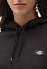 Juodas medvilninys bliuzonas su kapuce, švelni tekstūra ir mažas siuvinėtas "Dickies" logotipas ant krūtinės.