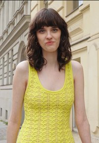 Top de renda amarelo com decote redondo, apresentando um padrão texturizado; usado com cabelo solto e ondulado e uma expressão neutra.