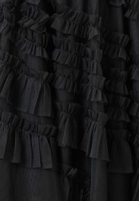 Țesătură neagră texturată, cu detalii pliate. Prezintă volane suprapuse, adunate, într-un design asemănător plaselor, creând profunzime și dimensiune.