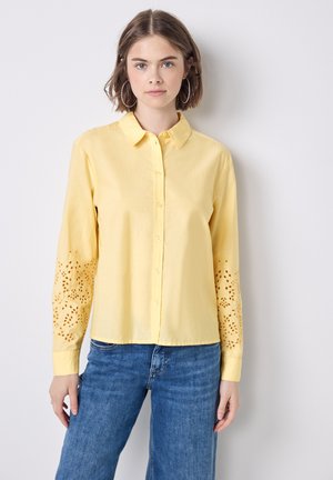 Blusa gialla in tessuto leggero con chiusura a bottoni, maniche lunghe con intricate velature e una vestibilità comoda.