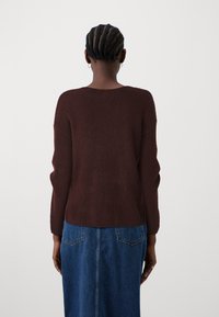 Burgunderfarbener Strickpullover mit geripptem Muster, rundem Halsausschnitt und langen Ärmeln, kombiniert mit einem blauen Jeansrock mit zwei Gesäßtaschen.