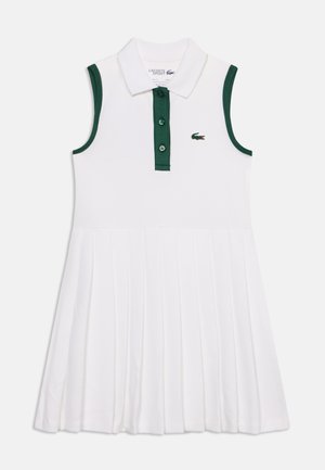 Robe polo blanche sans manches avec bordure verte aux emmanchures et patte de boutonnage, jupe plissée et petit logo crocodile sur la poitrine.