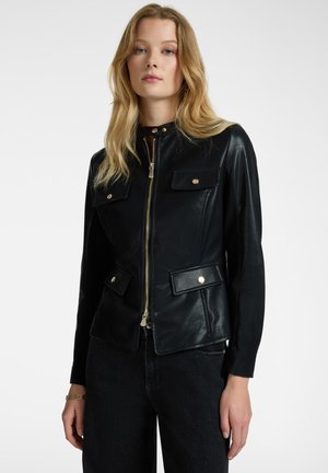 Giacca in pelle nera con chiusura a zip, colletto alto, due tasche frontali e hardware dorato. Texture liscia, design aderente.