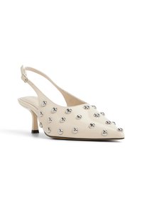 Beige, kiiltävästä nahasta valmistetut slingback-korkokengät, joissa on terävä kärki, niittikoristeet ja hoikka keskipohja, sekä solkiremmi nilkassa.
